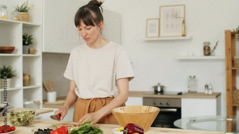 Young Caucasian woman cutting fresh vegetables at kitchen table while cooking salad for dinner