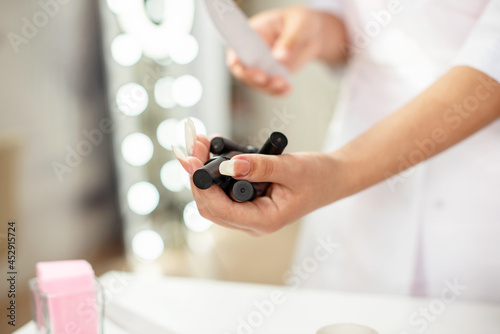 Female hands holding bottles of nail polish at beauty salon, close up with copy space, background with lights, nail polish presentation for manicure blog, online manicure course