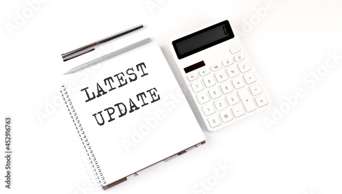 Notepad with text LATEST UPDATE with calculator and pen. White background. Business concept