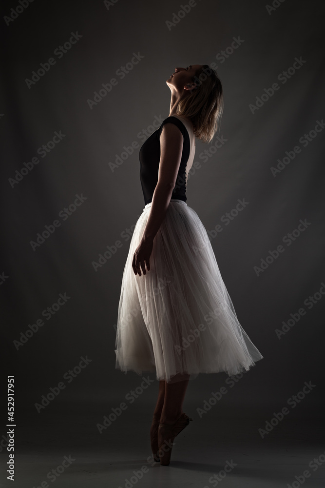ballerina with a white dress and black top posing on gray background.