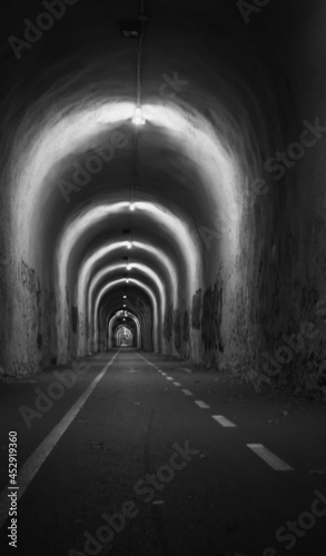 Narrow tunnel with light  monochrome. Empty tunnel with illumination  black and white. Travel destinations concept. Entrance to the tunnel. Interior of pedestrian tunnel.