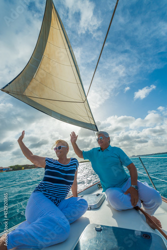 Romantic smiling senior couple enjoying sailing trip on a luxury summer holiday vacation, sunset and ocean in background, love and romance on a beautiful yacht, waving © TRAVEL EASY