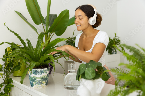 Ethnic woman in headset touching Asplenium leaves in house garden photo