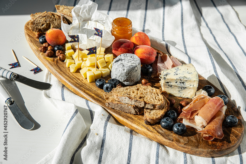 Cheese platter with different cow and goat cheeses, meat, nuts, Summer fruits and berries, jam and rye bread on wooden board.on white table.