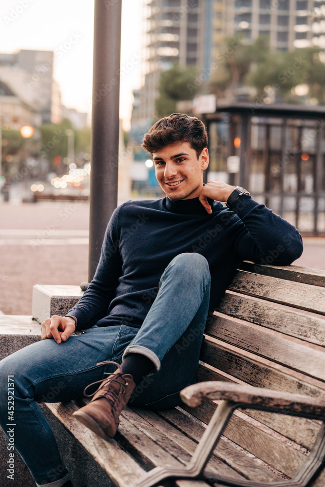 Cheerful trendy man sitting on bench in city Cheerful trendy man sitting on bench in city