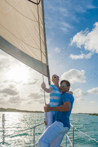 Romantic smiling young couple enjoying sailing trip on a luxury summer holiday vacation, sunset and ocean in background, love and romance on a beautiful yacht