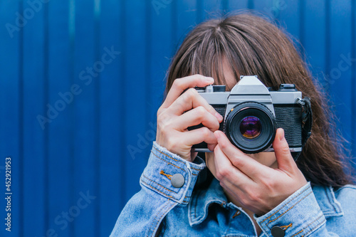 Unrecognizable woman taking photo on retro camera against blue wall photo