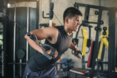 Young man Doing Heavy Weight Exercise For Chest On Machine With Cable In The Gym.Strong young sportsman in activewear pulling down handle of sports equipment while training. © Sirichai