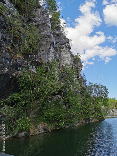 View from below of the marble beach, overgrown with trees and the emerald water of the Marble Canyon in the Ruskeala Mountain Park on a sunny summer day. © Elena