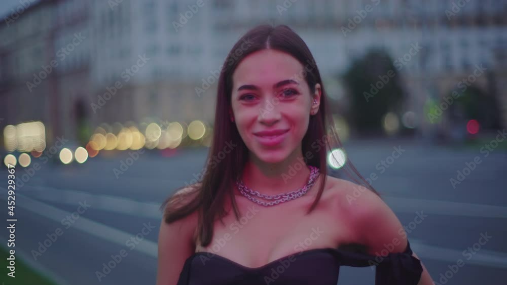 Elegant woman in black dress smiling while looking at camera in pink
