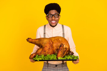Photo portrait man in glasses keeping baked chicken on thanksgiving day smiling isolated bright yellow color background
