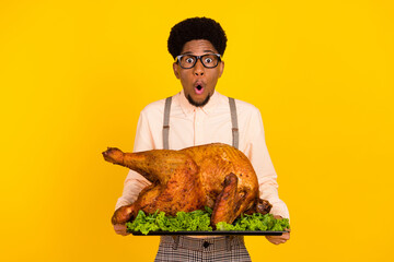 Photo portrait man in glasses keeping baked chicken on thanksgiving day amazed isolated vivid yellow color background