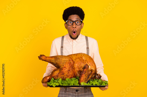 Photo portrait man in glasses keeping baked chicken on thanksgiving day amazed isolated vivid yellow color background