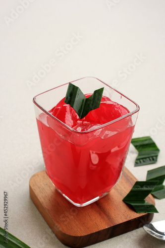 Manisan Kolang-Kaling (Preserved Sugar Palm Fruit) with Red Color. Served in a Glass with Wooden Coaster and Pandan Leaves as Garnish. This Dessert is Indonesian Typical Refreshment photo