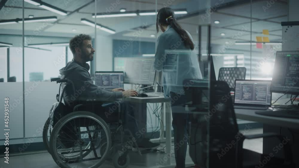 Disability-Friendly Office: Happy IT Programmer with Disability in a Wheelchair Talks with Colleague while Working on Computer. Software Engineers Develop Innovative App, Program. Medium Shot Disability-Friendly Office: Happy IT Programmer with Disability in a Wheelchair Talks with Colleague while Working on Computer. Software Engineers Develop Innovative App, Program. Medium Shot