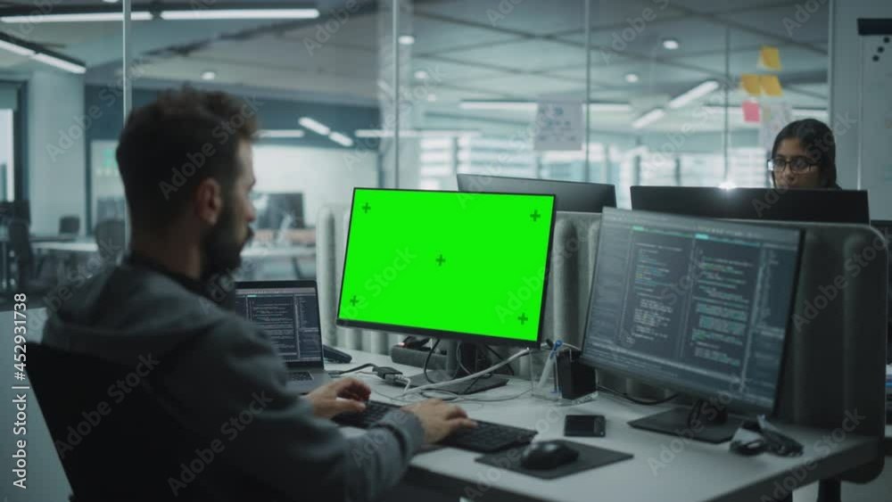 Multi-Ethnic Office: IT Programmer Working on Computer with Green Screen Chroma Key Display. Male Software Engineer Developing App, Program, Video Game. Terminal with Code Language. Over Shoulder Shot Multi-Ethnic Office: IT Programmer Working on Computer with Green Screen Chroma Key Display. Male Software Engineer Developing App, Program, Video Game. Terminal with Code Language. Over Shoulder Shot
