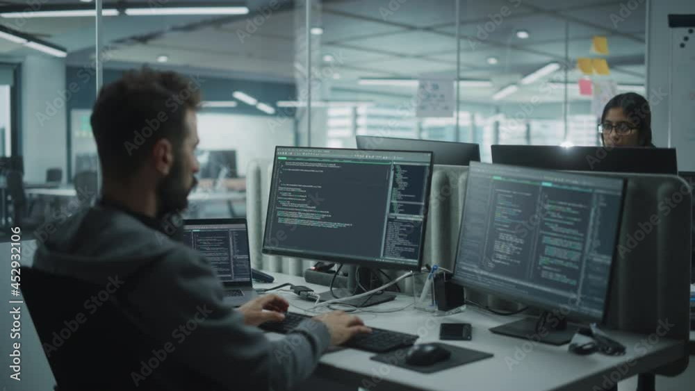 Diverse Office: IT Programmer Working on Desktop Computer. Male Specialist Creating Innovative Software Engineer Developing App, Program, Video Game. Terminal with Coding Language. Over Shoulder Diverse Office: IT Programmer Working on Desktop Computer. Male Specialist Creating Innovative Software Engineer Developing App, Program, Video Game. Terminal with Coding Language. Over Shoulder