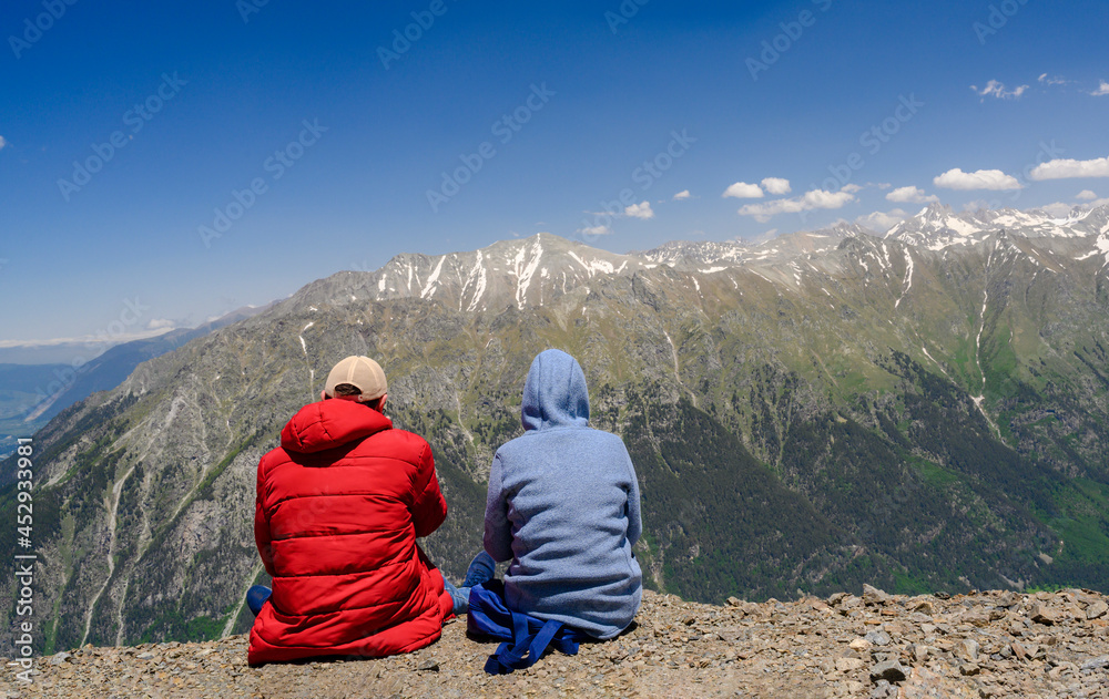 A couple of young people high in the Dombay Mountains, covered with snow, admires the view