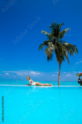 Elegant sexy woman in the white bikini on the sun-tanned slim and shapely body is posing near the swimming pool on Maldives island. Perfect body bikini model in luxury resort on Maldives.Luxury travel