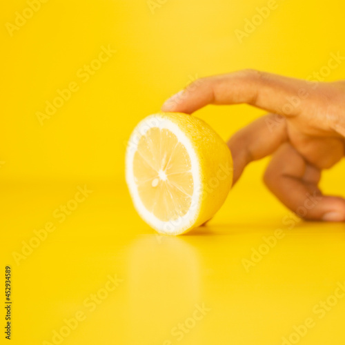 Female finger squeezing half of lemon on yellow background