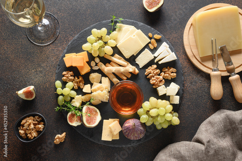 Cheese platter with grapes, nuts, figs on a brown background. Festive appetizer for party. View from above.