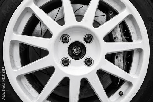 The detail of a wheel of a rallye car with part of the rim, brake caliper and brake disc visible. Black and white edit. 