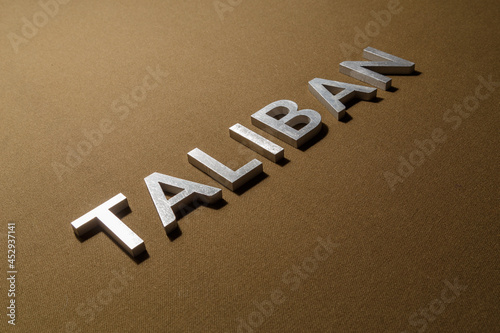the word taliban laid with silver metal letters on rough tan khaki canvas fabric photo