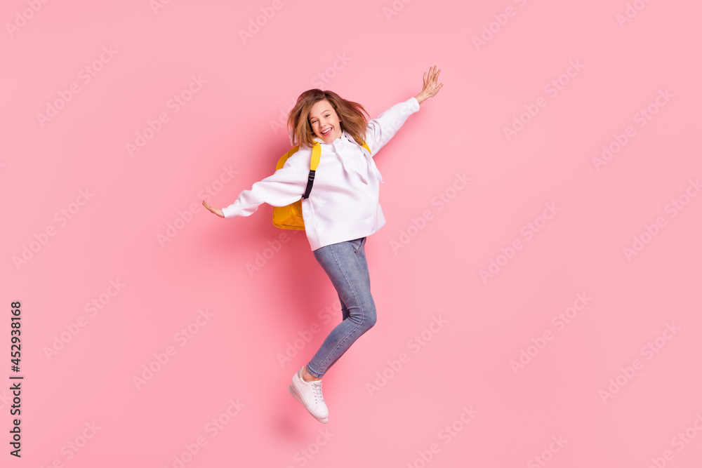 Full length body size girl wearing white hoodie jumping up with backpack isolated pastel pink color background Full length body size girl wearing white hoodie jumping up with backpack isolated pastel pink color background
