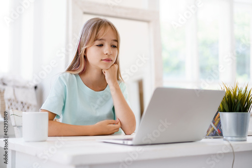 Happy little girl pupil using laptop at home
