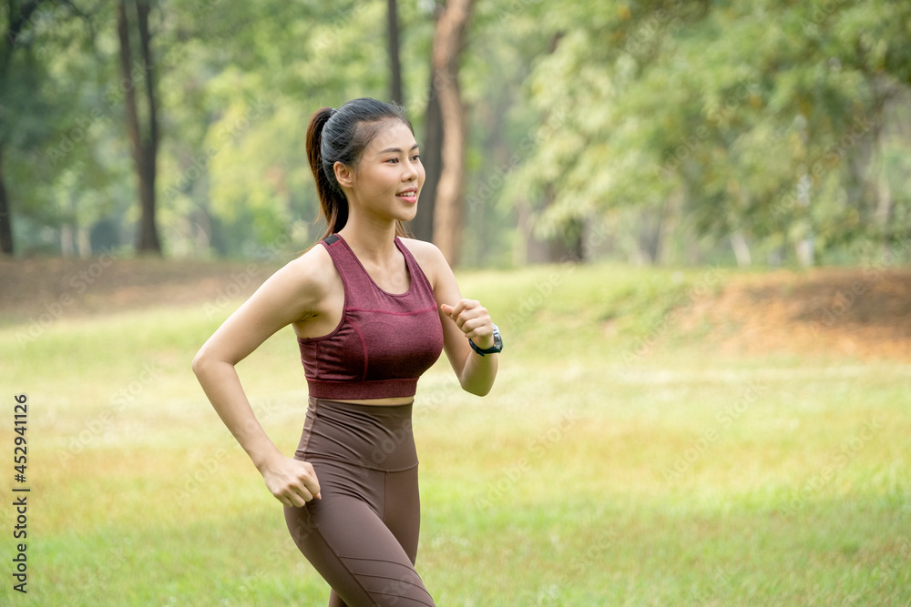 Close up Asian woman jogging in park or garden with green field and tree as background during morning time. Close up Asian woman jogging in park or garden with green field and tree as background during morning time.