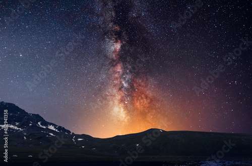 Beautiful night landscape, snow-capped mountains and hill, starry sky with bright milky way galaxy. Night landscape. Astronomical background, night scene.