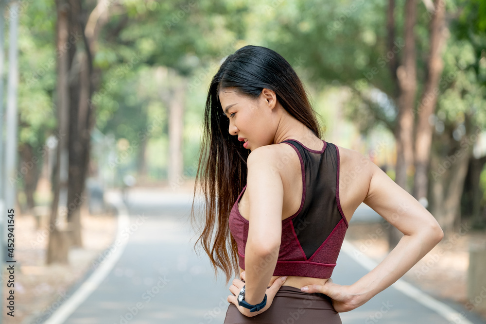 Back of Asian sport woman show action of waist or back pain after exercise in park or garden with day light. Back of Asian sport woman show action of waist or back pain after exercise in park or garden with day light.