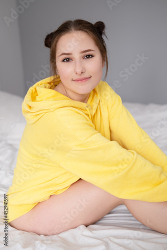 cheerful positive brunette woman in yellow hoodie in white bedroom on bed with white linens. happy people. millennial generation. fashionable teenager © OliaVesna