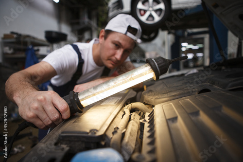 Selective focus on a lamp in the hand of car repairman at the garage