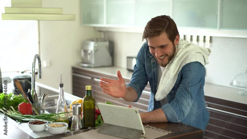 Man following recipe on tablet and cooking tasty food in kitchen at home Man following recipe on tablet and cooking tasty food in kitchen at home