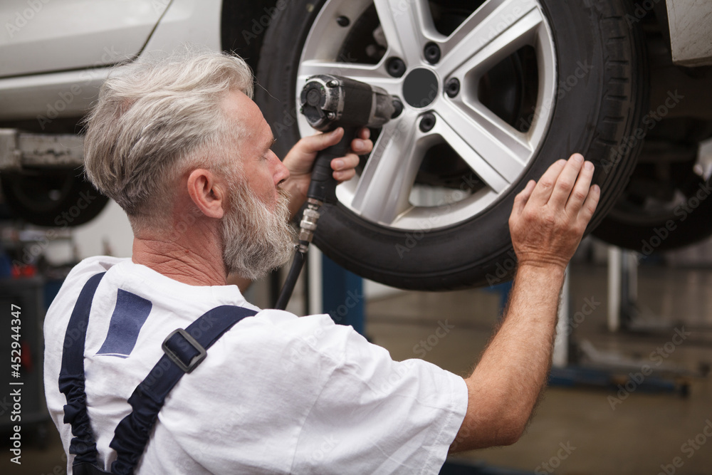 Rer view shot of a senior mechanic repairing wheels of an auto on car lift Rer view shot of a senior mechanic repairing wheels of an auto on car lift