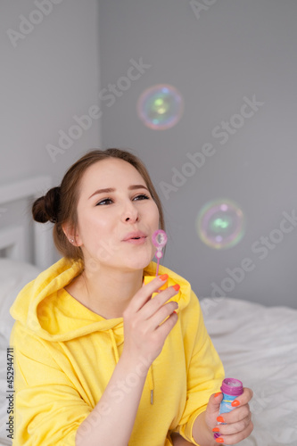portrait of charming young woman in yellow among soap bubbles on bright grey background. fashionable teenager. trendy colours.