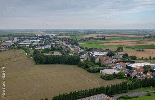 Diksmuide, Flanders, Belgium - August 3, 2021: Aerial view on wide agricultural landscape NW of Ijzertoren under Light blue sky. Industry zone and church of Kaaskerke village along N35. © Klodien
