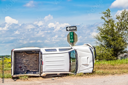 Canvas Print White long cab pick up truck turned on its side in a wreck at an intersection in the country beside a stop sign