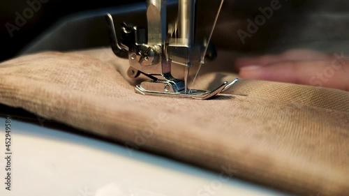Sewing Machine Needle in Motion. Close-up of sewing machine needle rapidly moves up and down. The tailor sews Brown fabric on the sewing workshop. The process of sewing fabric.