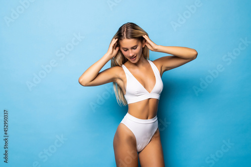 Cropped image of fitness young woman in underwear showing sexy fit body standing posing hold hands on hips legs isolated on pastel blue colour background, studio portrait © F8  \ Suport Ukraine