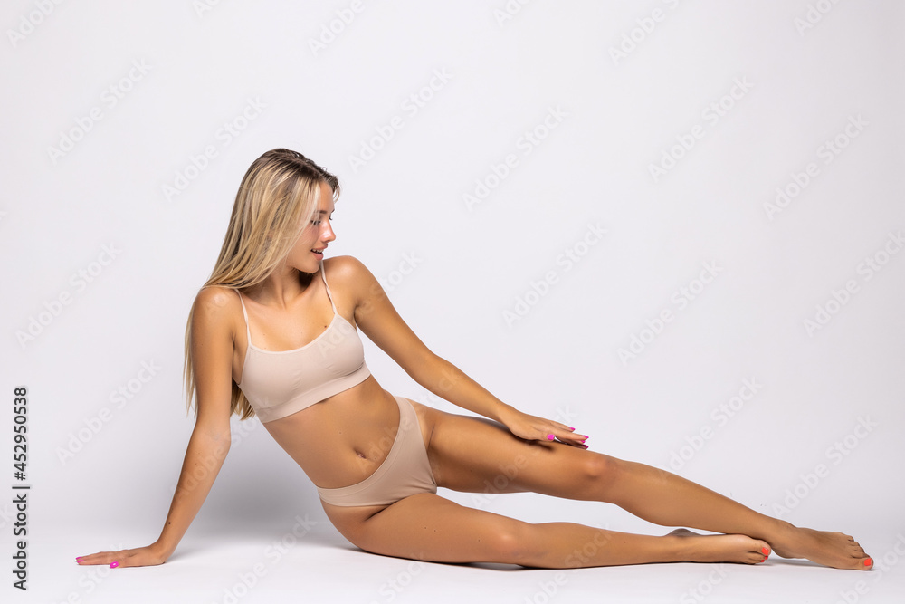 Young woman wearing beige lingerie while being on the floor isolated on white background