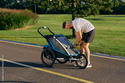 Young father is walking with his son in a baby carriage at city park. Dad with child pram outdoor workout