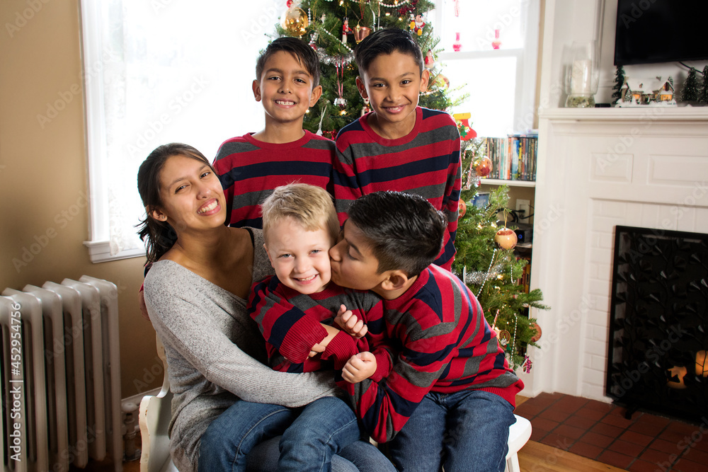 Indoor casual family Christmas portrait of five siblings in matching clothing smiling and having fun with tree in background