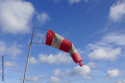 Close up of red and white windsock indicator on blue sky with many white clouds background.
