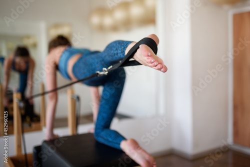 A young woman in sportswear does Pilates on a reformer, lifting her leg up