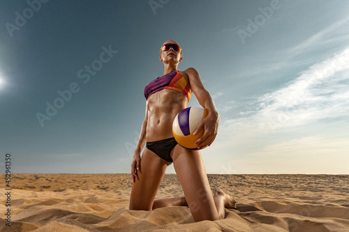 Fotografija Girl athlete volleyball player on the beach playing at sunset