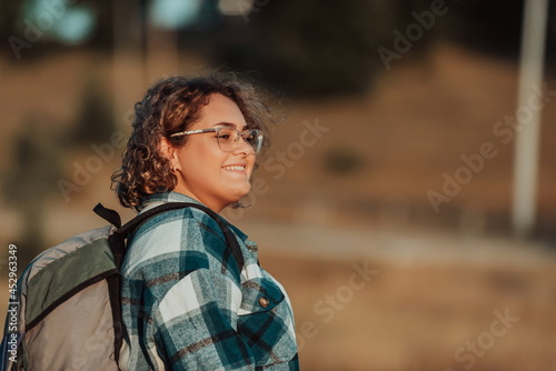 Front view of woman hiker standing outdoors in nature at sunset.