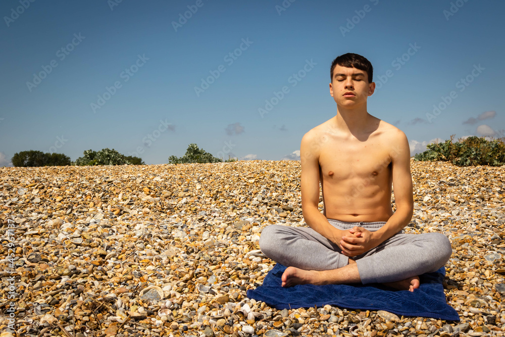 Teenage boy on a beach meditating