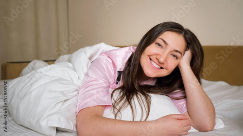 Nice brunette woman in pajama smiles gently and sincerely showing air kisses to coming husband lying on king size bed in bedroom close view